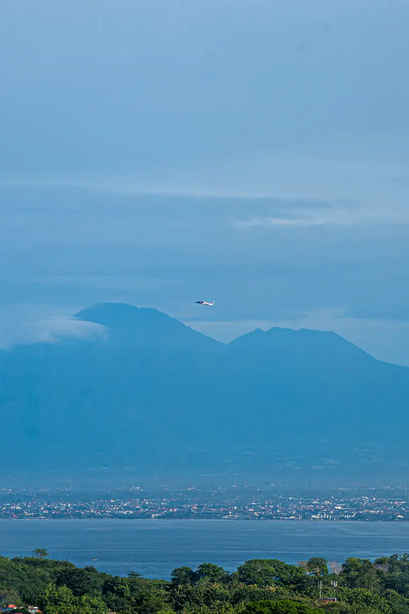 Pesawat melintas dengan latar siluet Gunung Agung